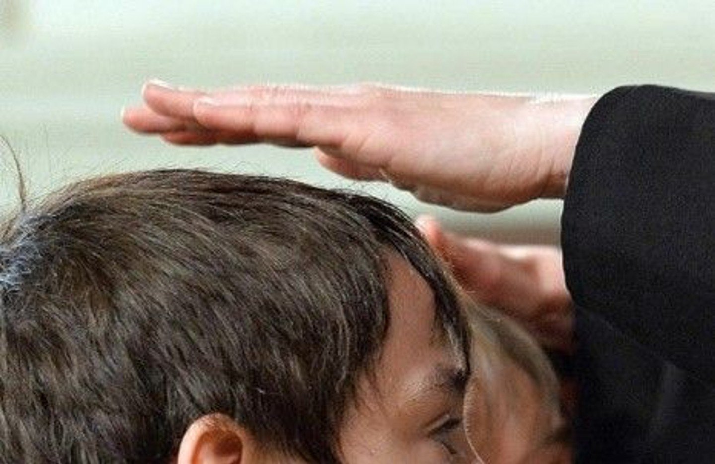 Man sieht die obere hälfte eines Kopfes mit kurzen, dunklen Haaren von der Seite und eine Hand zum Segen über den Kopfgehalten.